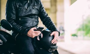 La imagen muestra a un motociclista revisando su teléfono celular.