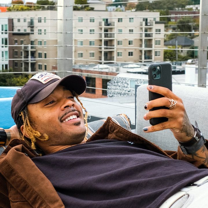 Un hombre, recostado en un balcón, sonríe mientras utliza su celular para enviar mensajes.