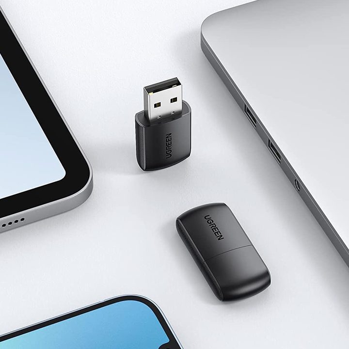 Adaptador de red de doble banda junto a otros equipos, como una portátil y un teléfono inteligente.