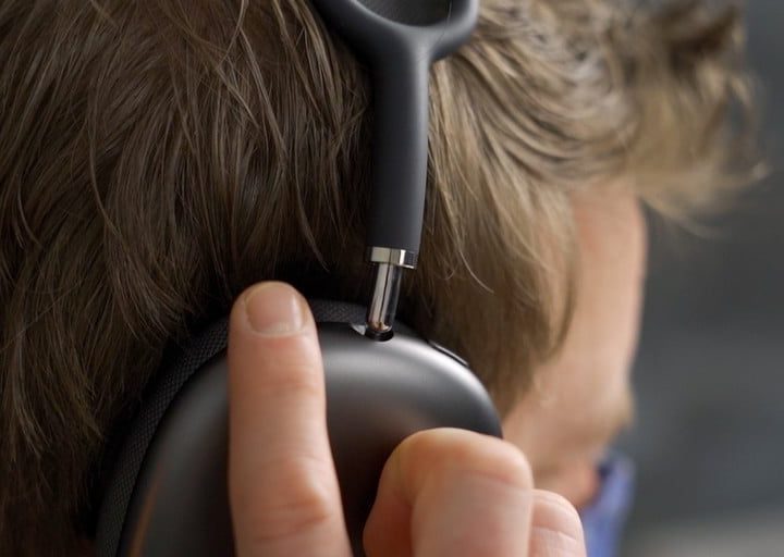 Una persona con unos AirPods Max color negro puestos en su cabeza y sosteniendo uno de ellos con una mano.