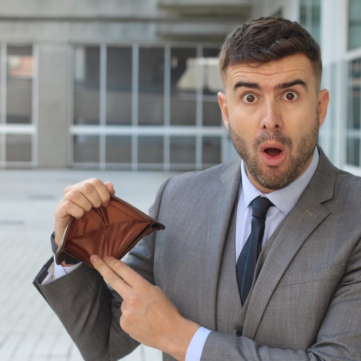 Un hombre de traje mira con preocupación mientras sostiene una billetera vacía sin dinero ni documentos.