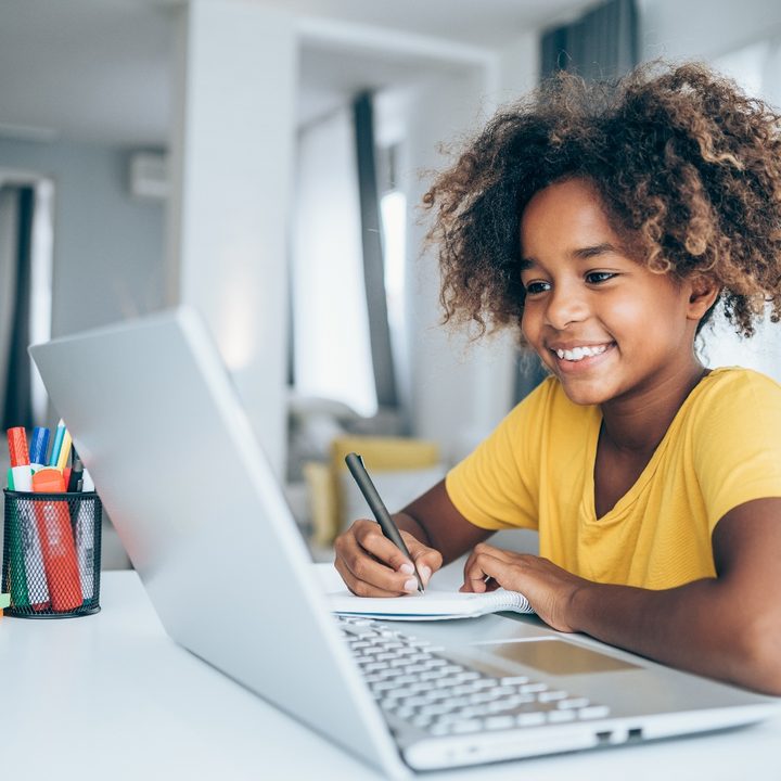 Una niña está sentada frente a una computadora en clases remotas.