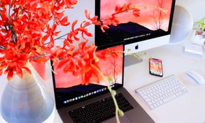 Un Macbook, un iMac , un iPhone y un teclado inalámbrico de Apple junto a un florero de colores vivos.