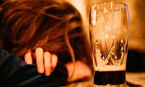 La imagen muestra la cabeza de una mujer apoyada al lado de un vaso con cerveza.