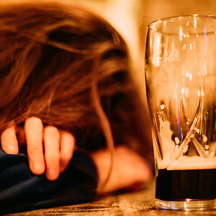 La imagen muestra la cabeza de una mujer apoyada al lado de un vaso con cerveza.