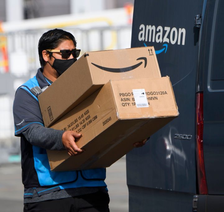 La imagen muestra a un trabajador de Amazon bajando unas cajas de un vehículo.