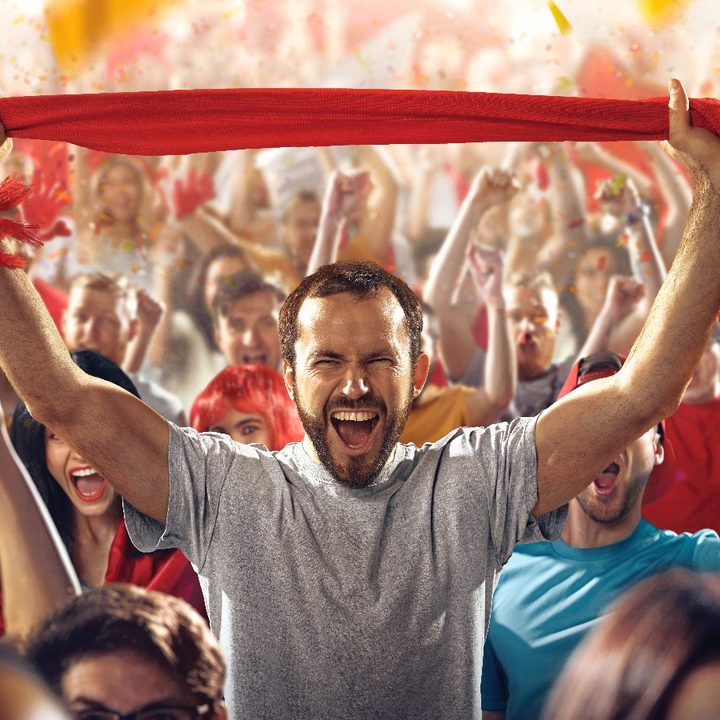 Un grupo de hinchas del fútbol en celebran en un estadio con una bufanda de color rojo