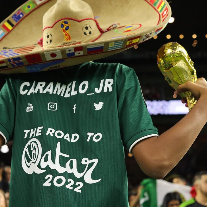 Un hincha mexicano usa una camiseta con el logo del mundial de Qatar mientras usa un sombrero mexicano y tiene en su mano una réplica del trofeo de la Copa del Mundo.