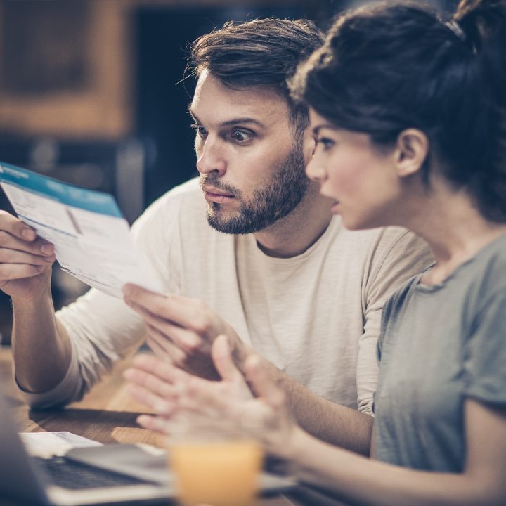 Un hombre y una mujer miran con cara de sorpresa y angustia una cuenta de impuestos.