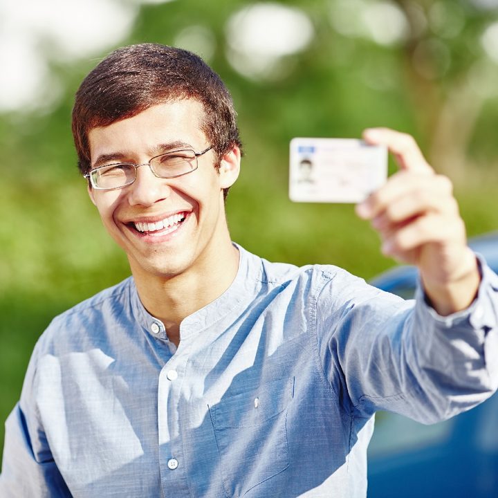 Una persona sonríe mientras muestra su licencia de conducir