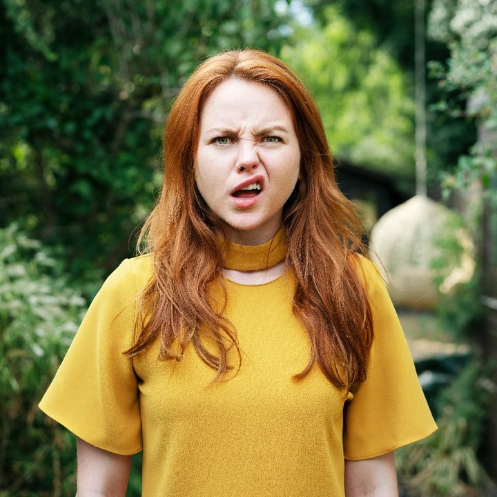 Una mujer colorina viste una polera amarilla con cara de pregunta