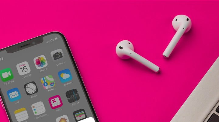 Unos AirPods sobre una superficie rosa junto a un iPhone.