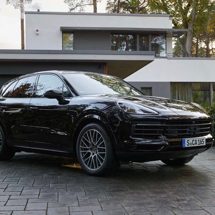 Vista frontal de dos cuartos de la Porsche Cayenne Platinum Edition 2022 en movimiento estacionada frente a una casa moderna.