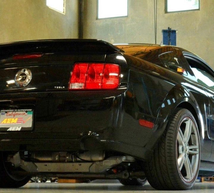 Vista de dos cuartos trasera de una Ford Mustang 2007 negro con tren motriz eléctrico de Tesla.