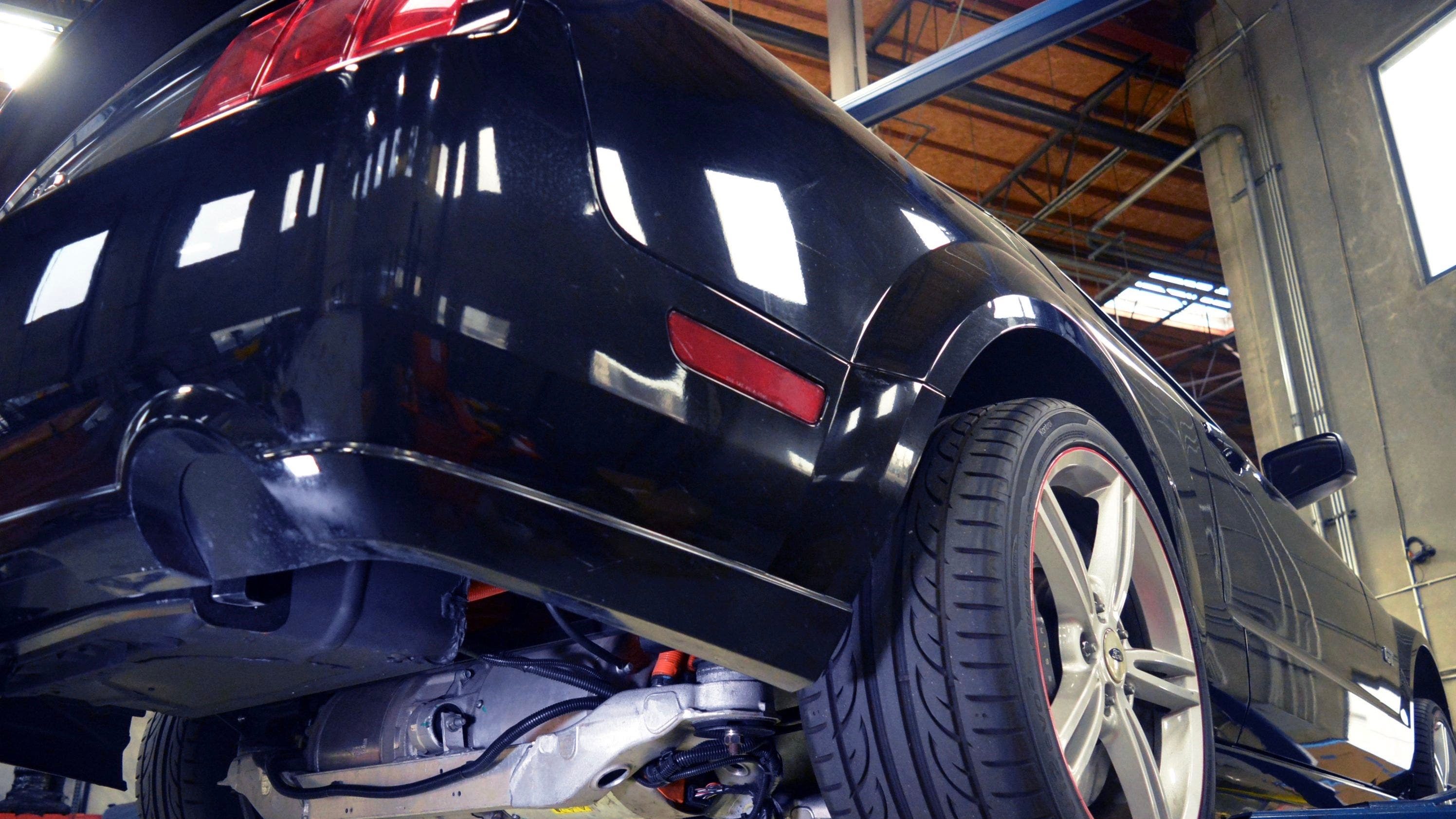 Vista de dos cuartos trasera de un Ford Mustang 2007 negro con tren motriz eléctrico de Tesla sobre un puente de reparaciones.