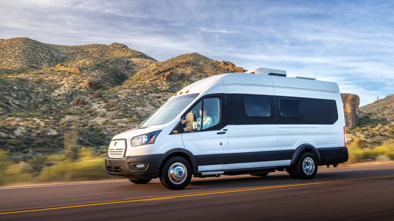 La imagen muestra a la Winnebago e-RV en color blanco circulando por una carretera con fondo de montañas.