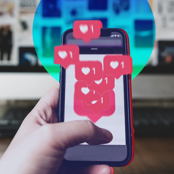 Una mano sosteniendo un celular, y dentro de este hay un montón de iconos Me Gusta de Instagram.