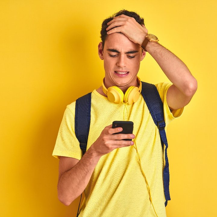 Un joven con camisa amarilla mira con cara de preocupación su teléfono