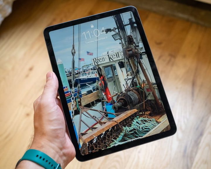 Un iPad Air 4 en la mano de una persona y al fondo un piso de madera.