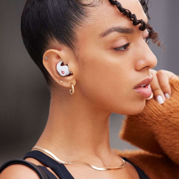 Audífonos Beats Fit Pro sobre una mesa de madera, junto a una computadora portátil.