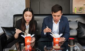 Una mujer y un hombre comen comida china para llevar sentados en un sofá.