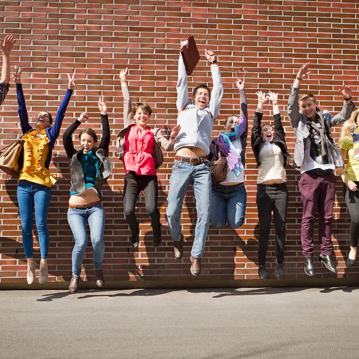Un grupo de estudiantes salta delante de una pared de ladrillos