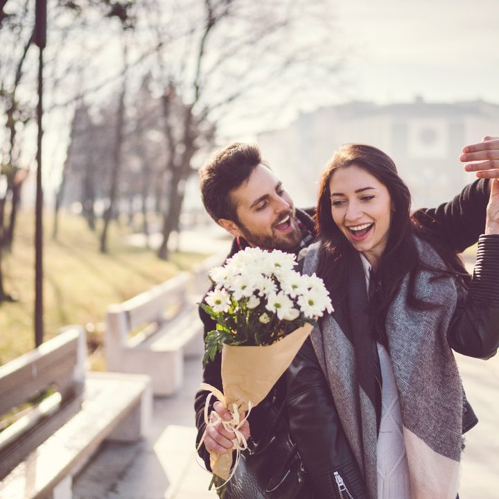 Un hombre sorprende con flores a una mujer mientras caminan por un parque