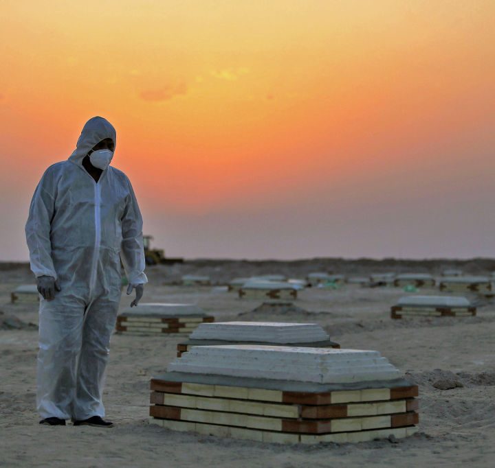 Una persona cubierta con un traje protector observa un ataúd en un terreno vacío.