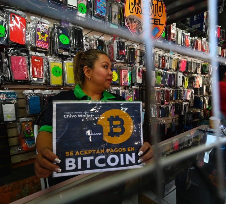 La imagen muestra a una mujer sosteniendo un letrero de Bitcoin en El Salvador.