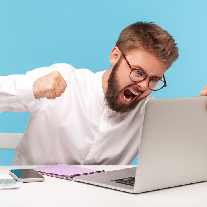 Un hombre molesto intenta pegarle a una computadora en una pieza con paredes celestes