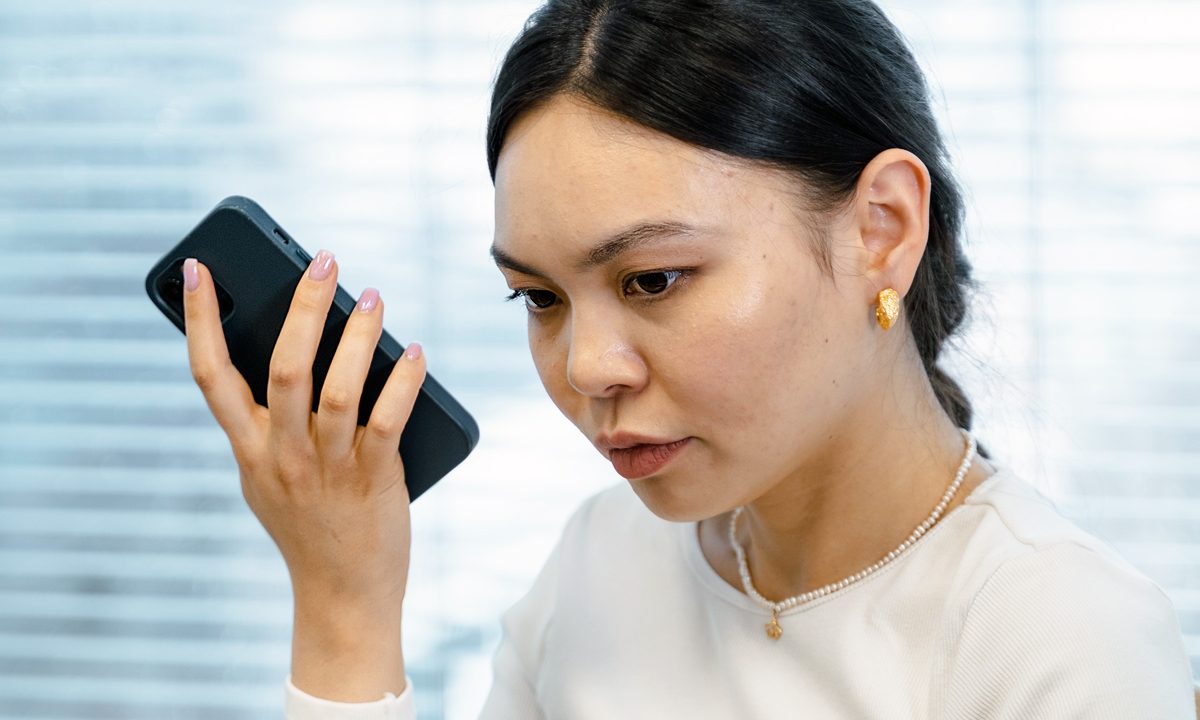 Una mujer escucha ell buzón de voz en un iPhone con expresión concentrada.