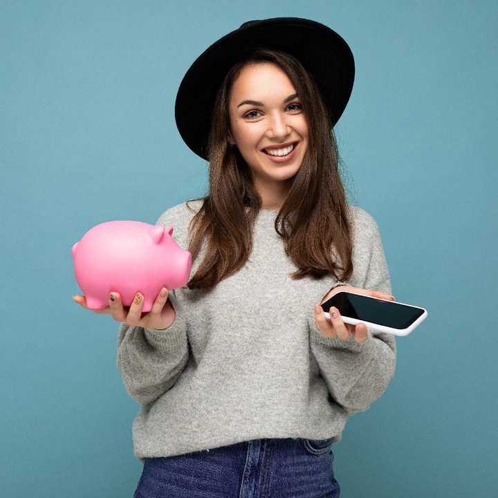 Una mujer sostiene sonríe mientras sostiene una alcancía y un teléfono