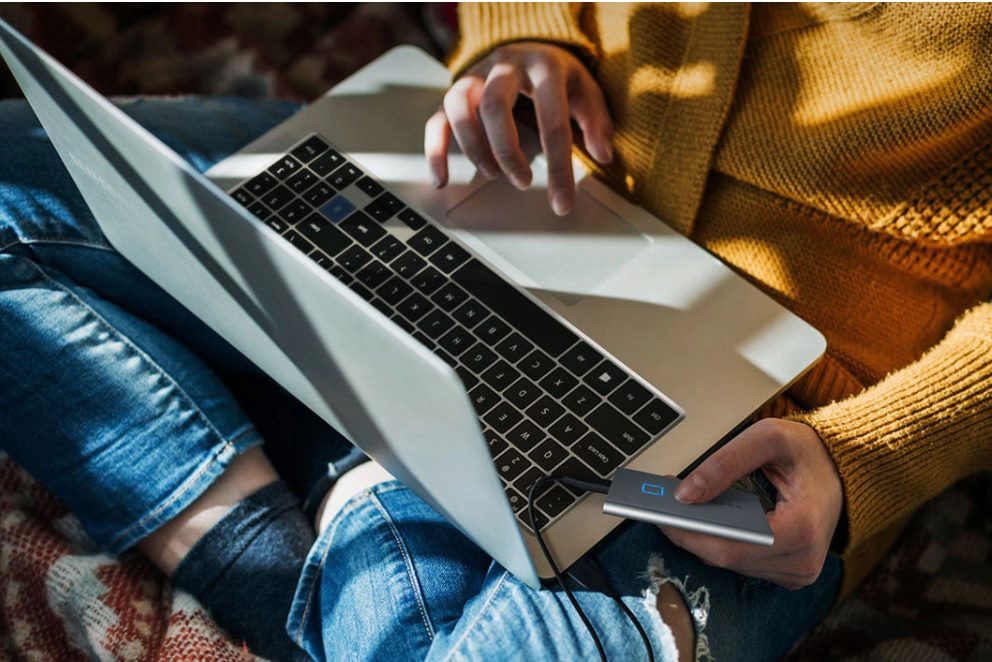 Una chica sentada con una laptop en sus piernas y conectado una unidad SSD Samsung T7.