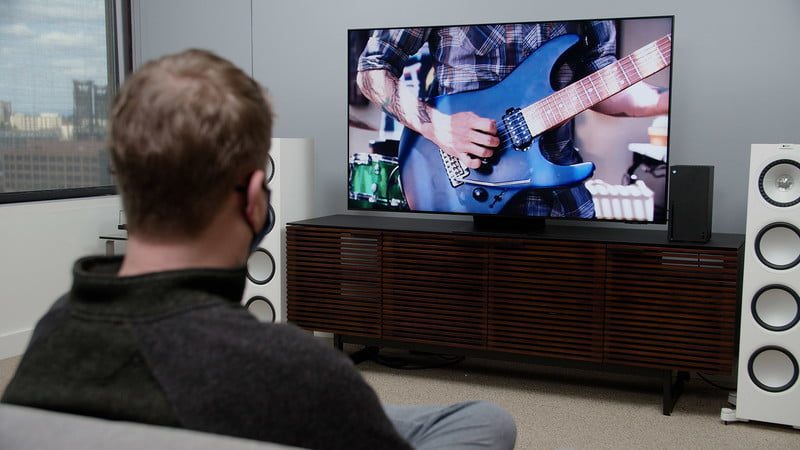 Un hombre ve a una persona tocar la guitarra eléctrica en televisión.