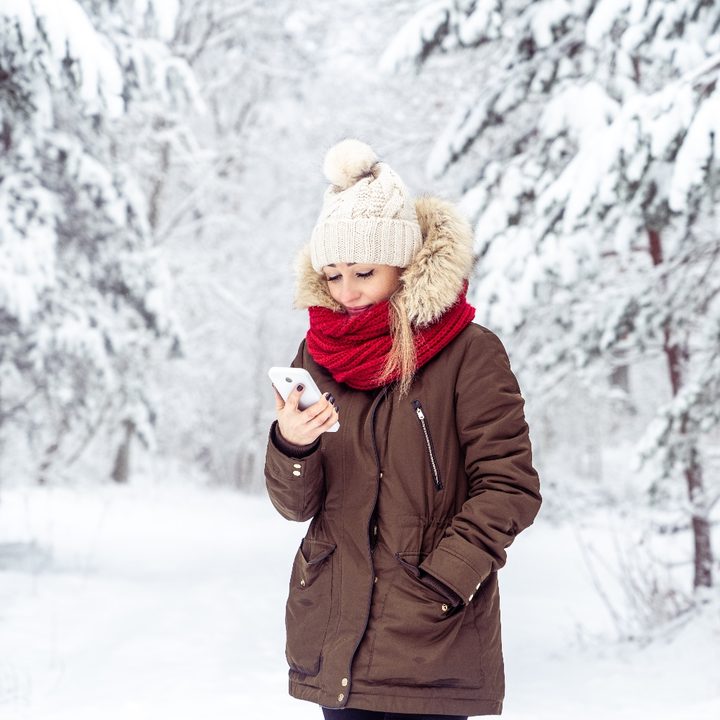 Una mujer sostiene un teléfono en un bosque con nieve
