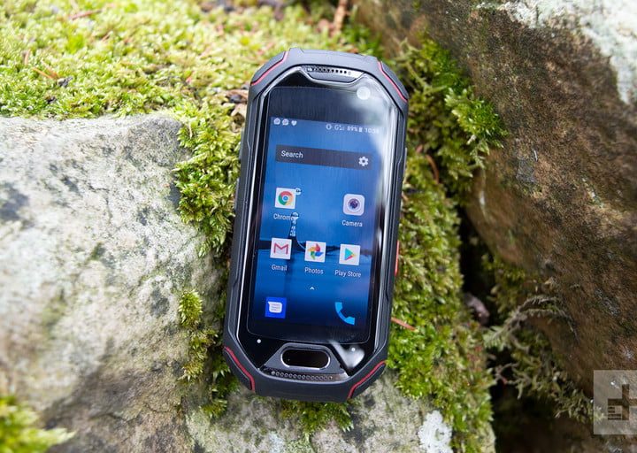 Unihertz Atom con pantalla azul sobre una roca con hierbas.