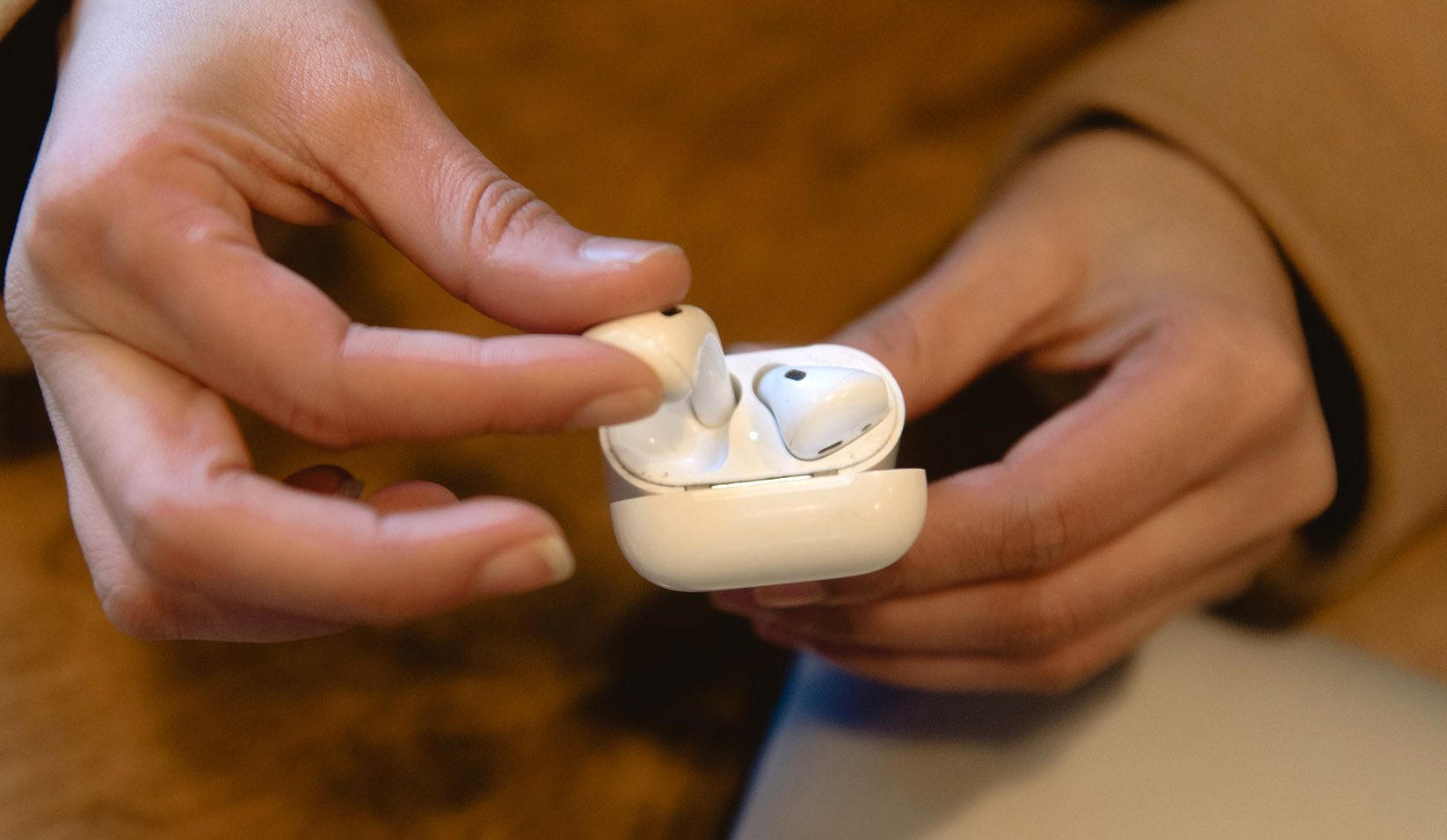 Un AirPod es sacado de sus estuche por las manos de una mujer.