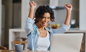 Una mujer levanta sus brazos en señal de celebración mientras trabaja en su computadora