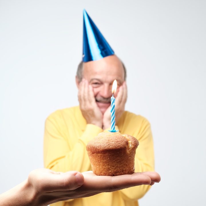 Una persona sostiene un queque con una vela para celebrar el cumpleaños de un hombre con gorro azul