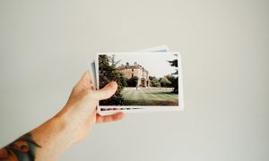 Una mano sostiene un montón de fotografías impresas frente a un fondo blanco.