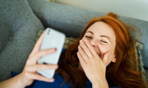 Una mujer ser ríe mientras observa su celular.