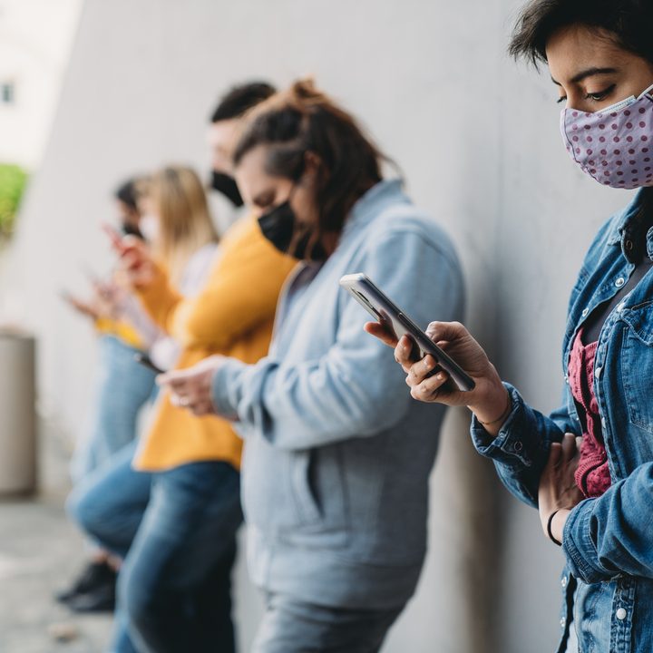 Varios jóvenes con mascarilla revisan sus smartphones.