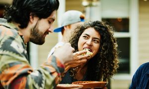 Una pareja de jóvenes mientras come tacos sobre unos platos.