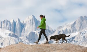 Una mujer camina junto a su perro por una montaña.