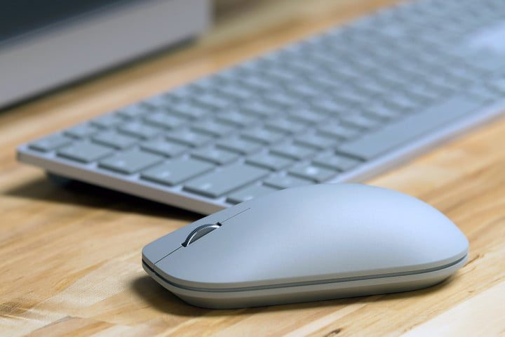 Microsoft Surface Mouse junto a un teclado sobre una superficie de madera.