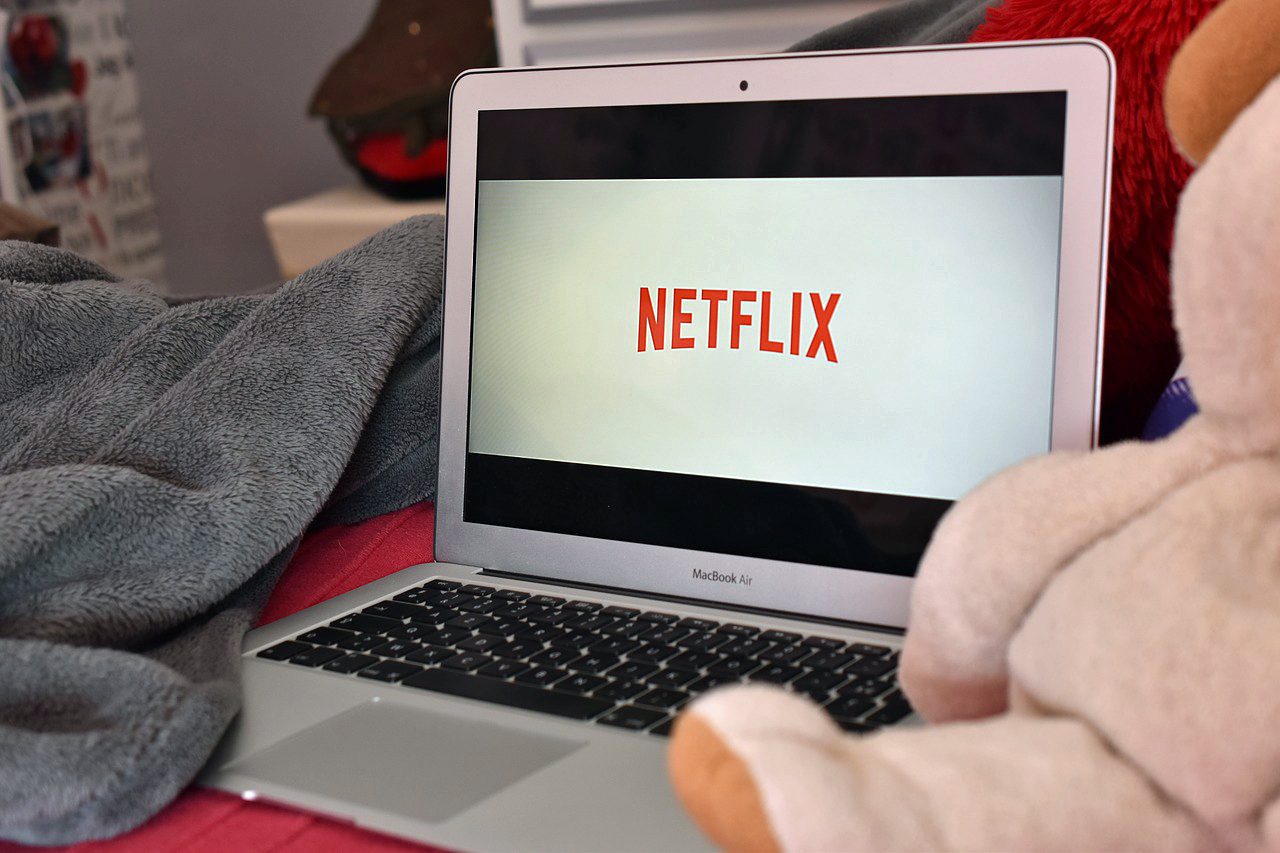 Una MacBook entre mantas y peluches mostrando el logo de Netflix en la pantalla.