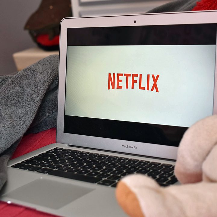 Una MacBook entre mantas y peluches mostrando el logo de Netflix en la pantalla.