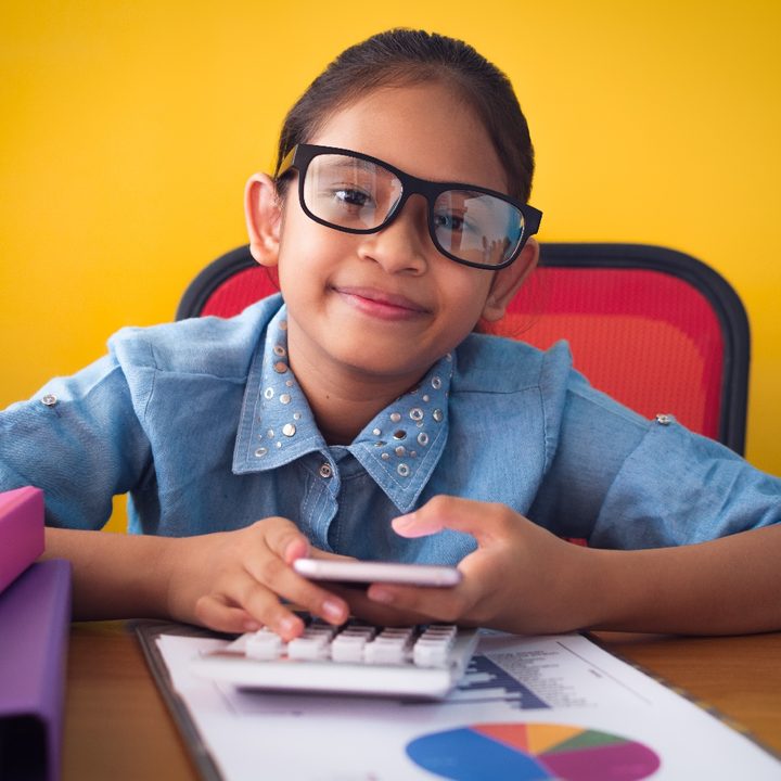 Una niña estudia sentada en un escritorio mientras sostiene un teléfono