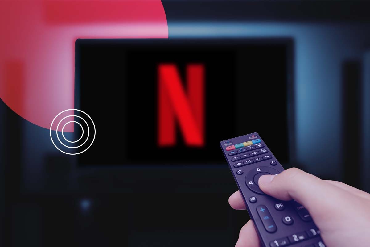 Una mano sosteniendo un control remoto y apuntando hacia el televisor con Netflix.