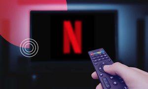 Una mano sosteniendo un control remoto y apuntando hacia el televisor con Netflix.